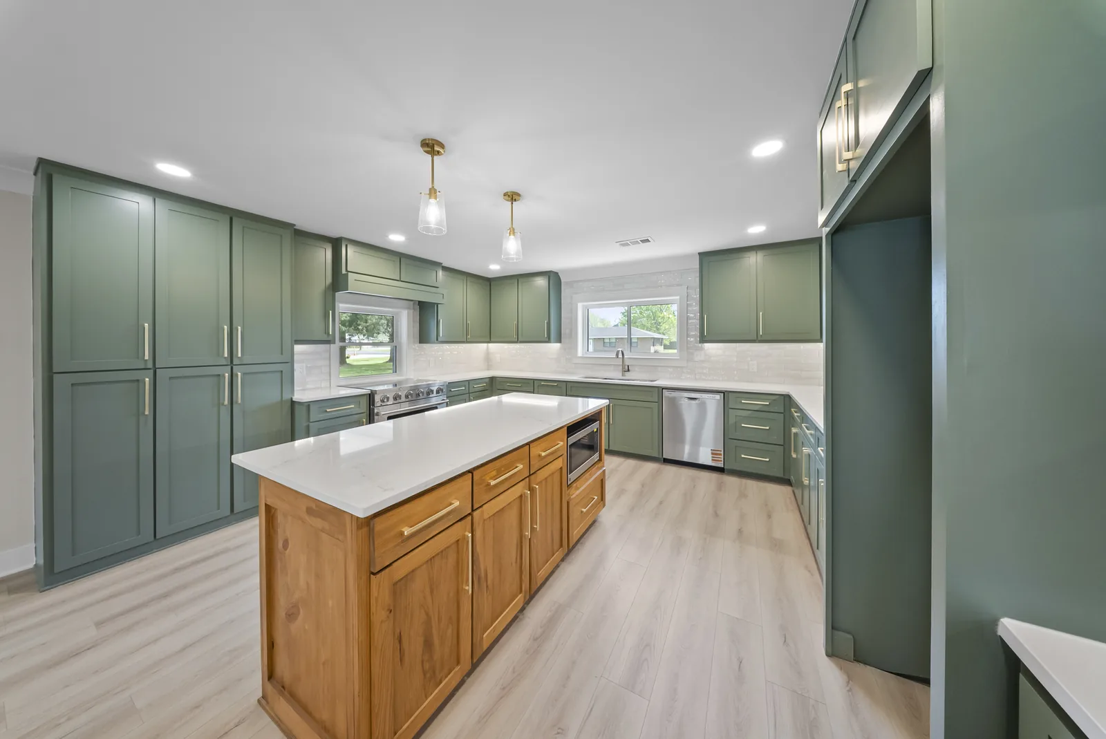 Completed kitchen with green custom cabinetry, brass details and a large island