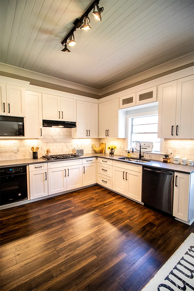 Bright remodeled farmhouse kitchen with white cabinetry and dark wood flooring