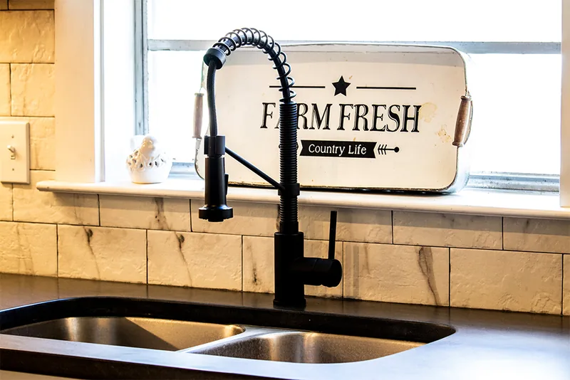 Black farmhouse sink faucet above a tiled kitchen backsplash